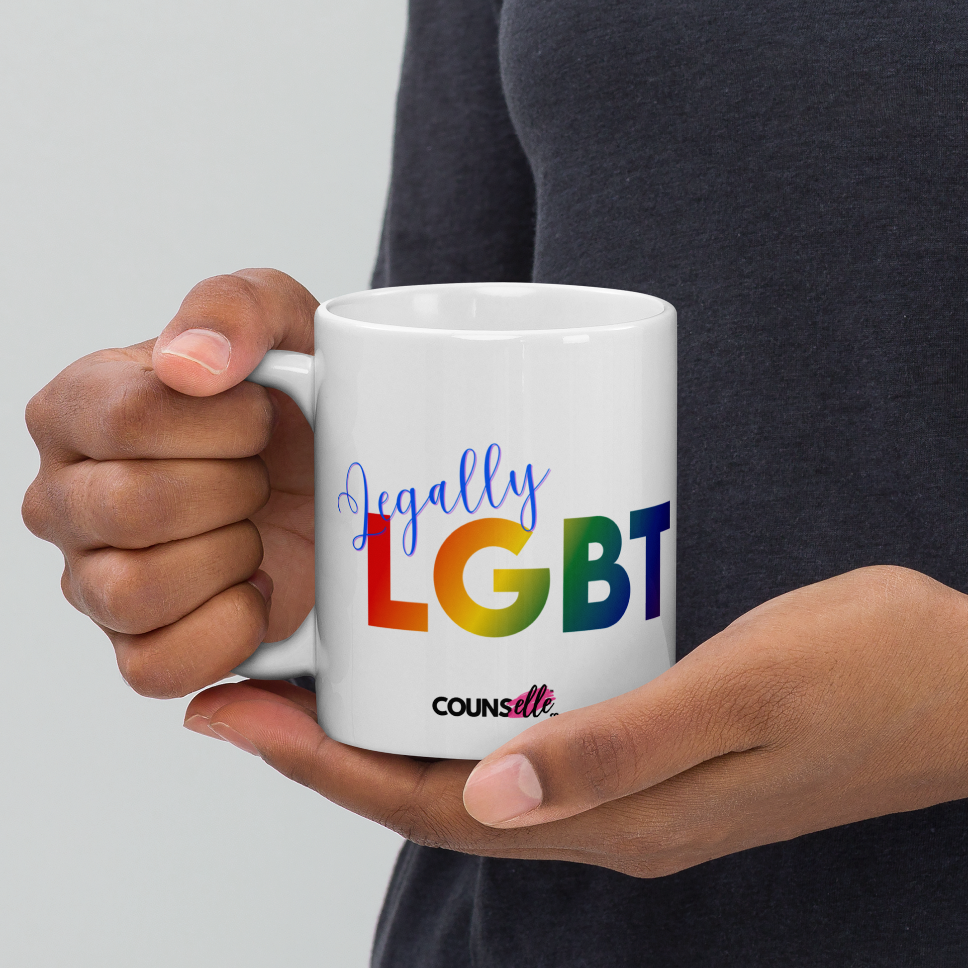 A person holding a white mug featuring the text "LGBT" in a rainbow-colored font, "Lawyer" in blue script, and the counsellecollection logo at the bottom  of the design.