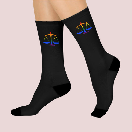 Side view of a pair of black crew socks featuring the rainbow justice scales design at the cuff.