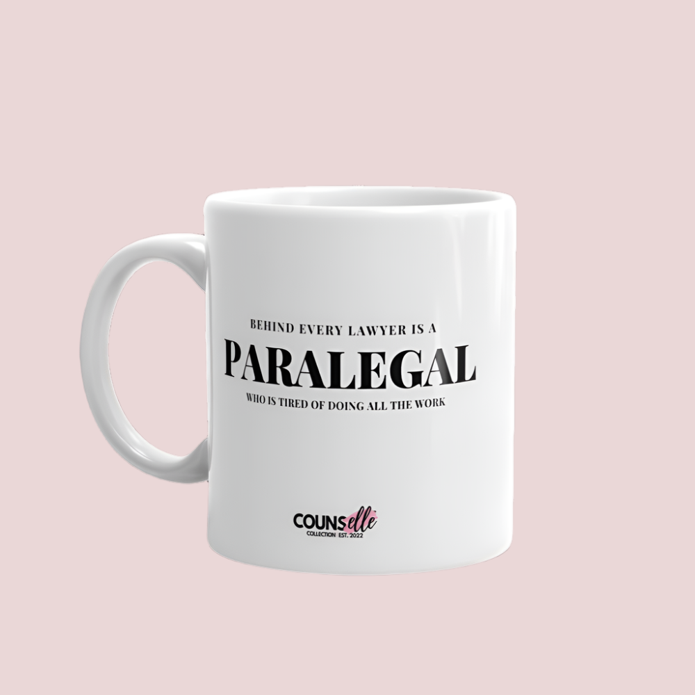 A white mug featuring the text "BEHIND EVERY LAWYER IS A PARALEGAL WHO IS TIRED OF DOING ALL THE WORK"