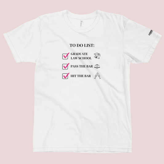 A white crewneck tee showing the text "TO DO LIST", with ticked-off boxes beside the texts "GRADUATE LAW SCHOOL" and an illustration of a graduation cap and diploma; "PASS THE BAR" and an illustration of justice scales; and "HIT THE BAR" and an illustration of clinking champagne flutes, with the counsellecollection logo on the left sleeve.