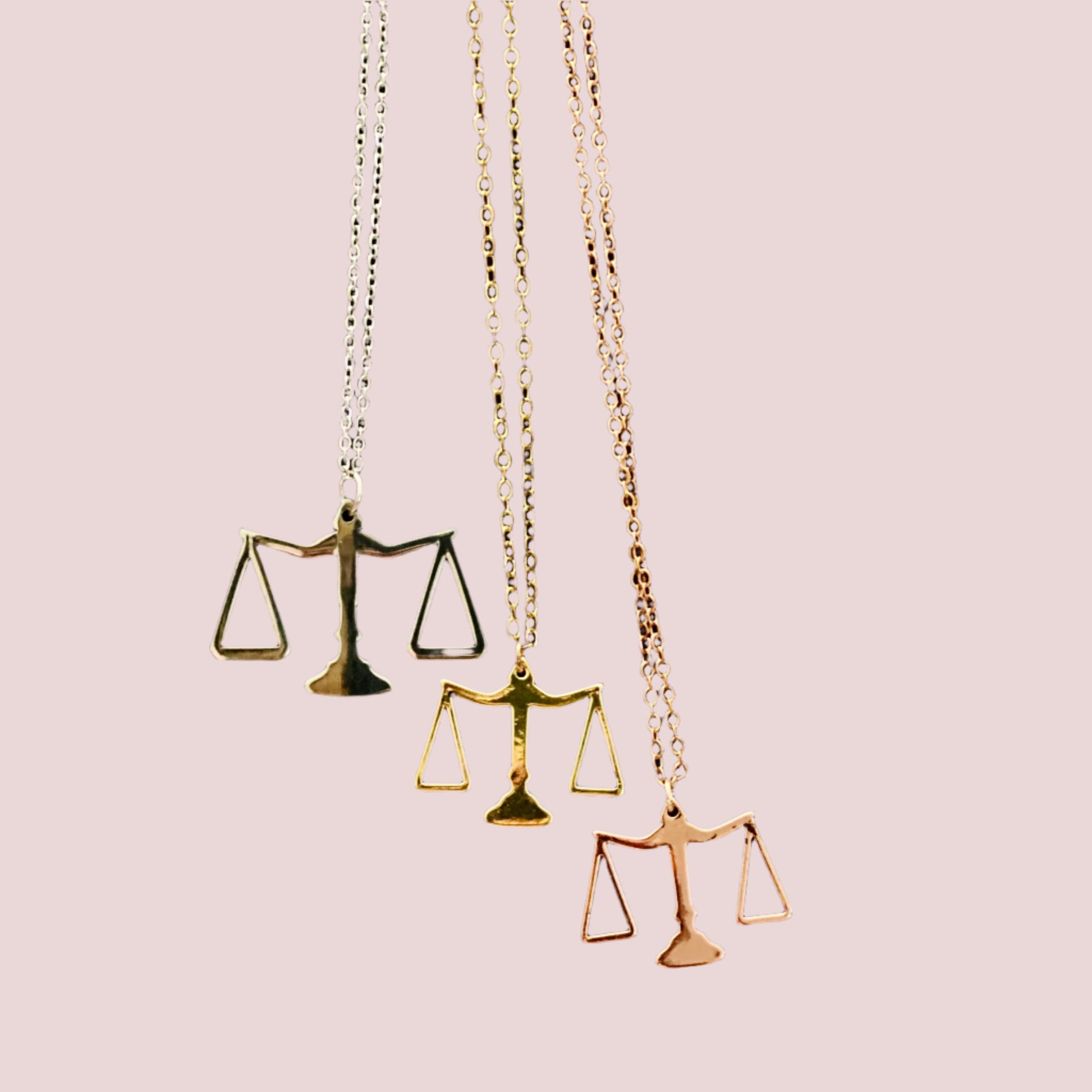 A stainless steel piece with 18k gold plating, featuring a sleek pendant in the shape of the scales of justice. Available in gold, rose gold, and silver.