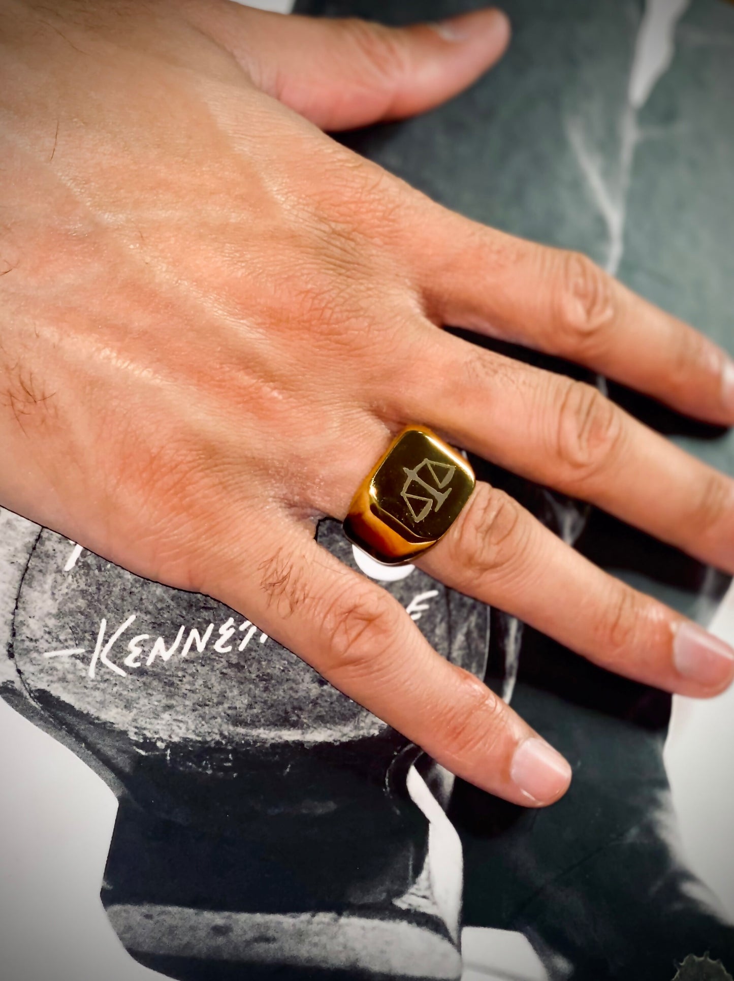 A sleek unisex ring featuring a justice scales emblem. Available in gold and silver.