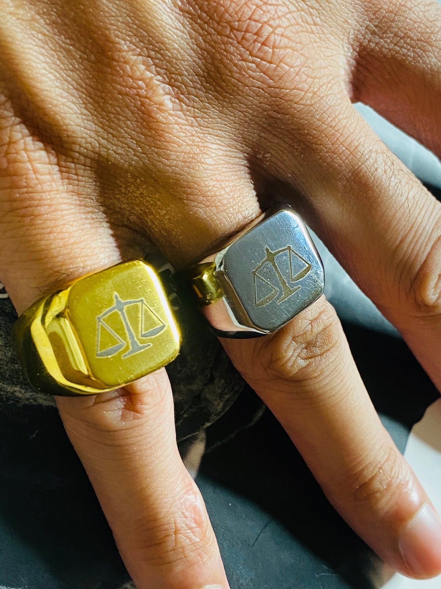 A sleek unisex ring featuring a justice scales emblem. Available in gold and silver.