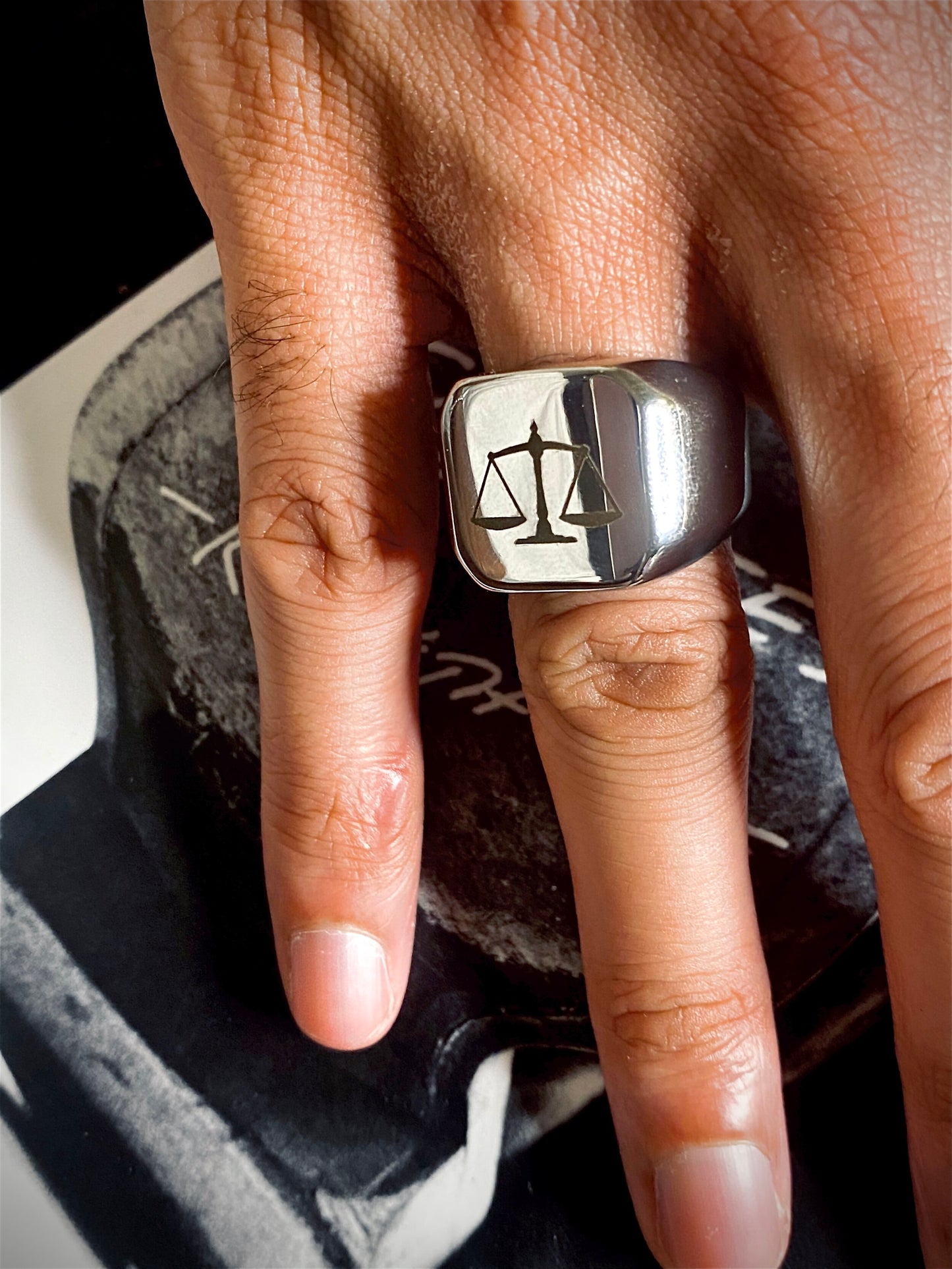 A sleek unisex ring featuring a justice scales emblem. Available in gold and silver.