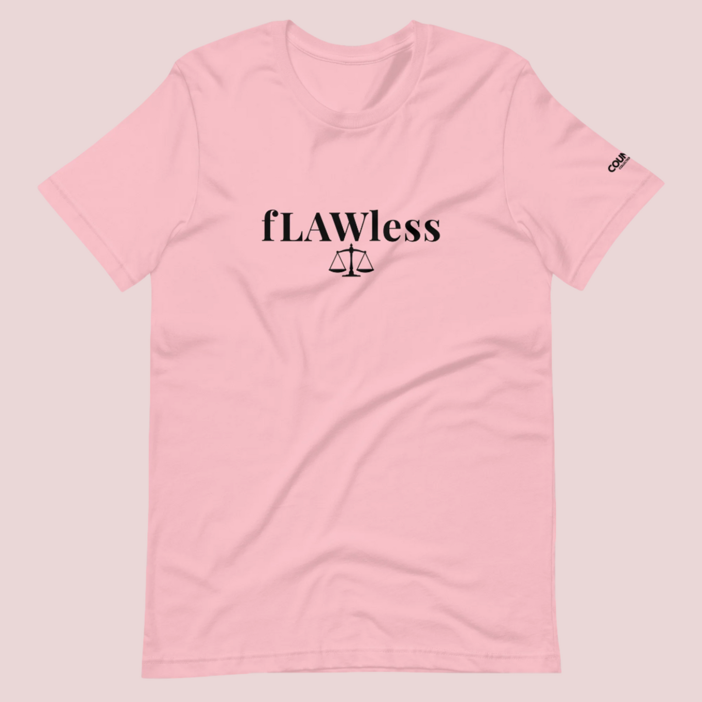A pink roundneck tee featuring the word "fLAWless", with the letters LAW in uppercase font, with an illustration of justice scales below. The counsellecollection logo is also seen on the left sleeve.