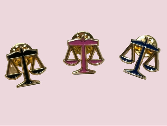 Three scales of justice lapel pins on a light pink background