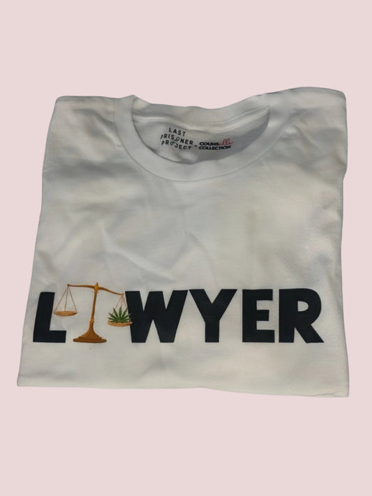 a white t-shirt, folded, with the word "LAWYER" in black text, with an unbalanced justice scale holding a cannabis leaf in place of the letter "A", symbolizing the unequal treatment of cannabis offenses under the law.