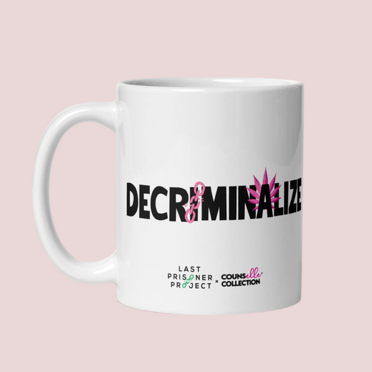 A white mug with the text "decriminalize" on the front. 

Last Prisoner Project and Counselle Collection® logos at the bottom of the mugs. 
