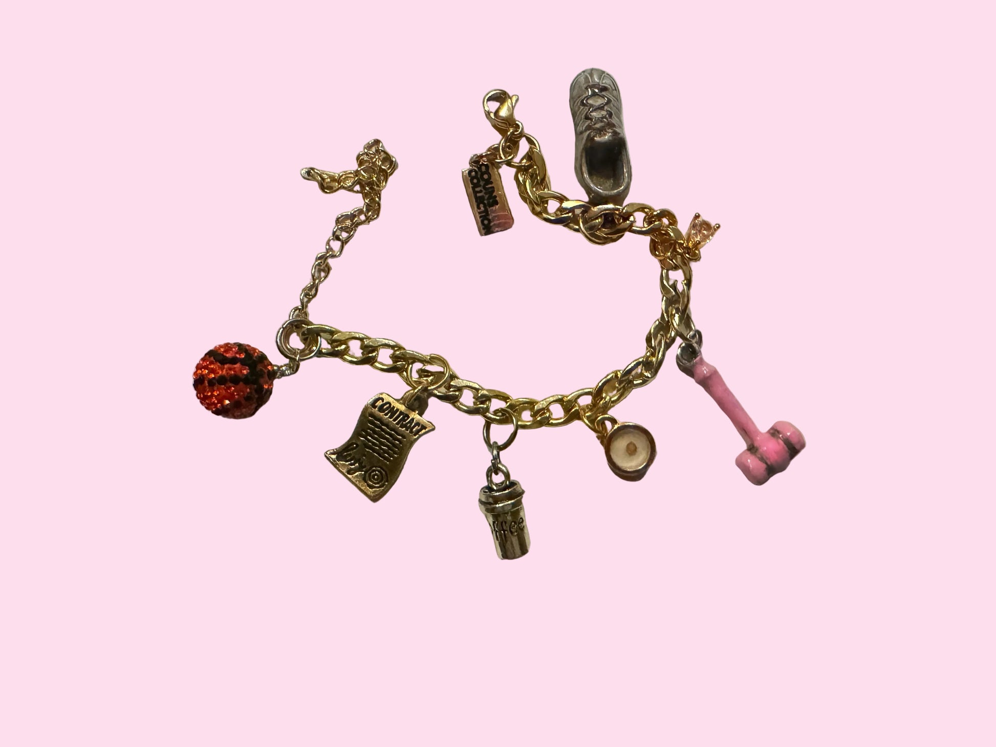 A gold-tone charm bracelet featuring various themed charms including a pink gavel, bedazzled basketball, signed contact, shoe, and other small icons