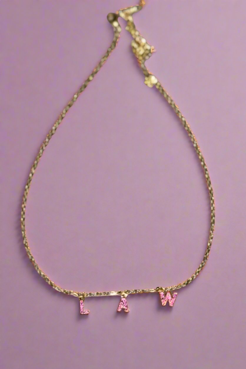 A gold necklace that spells the word LAW with pink stones on the letters