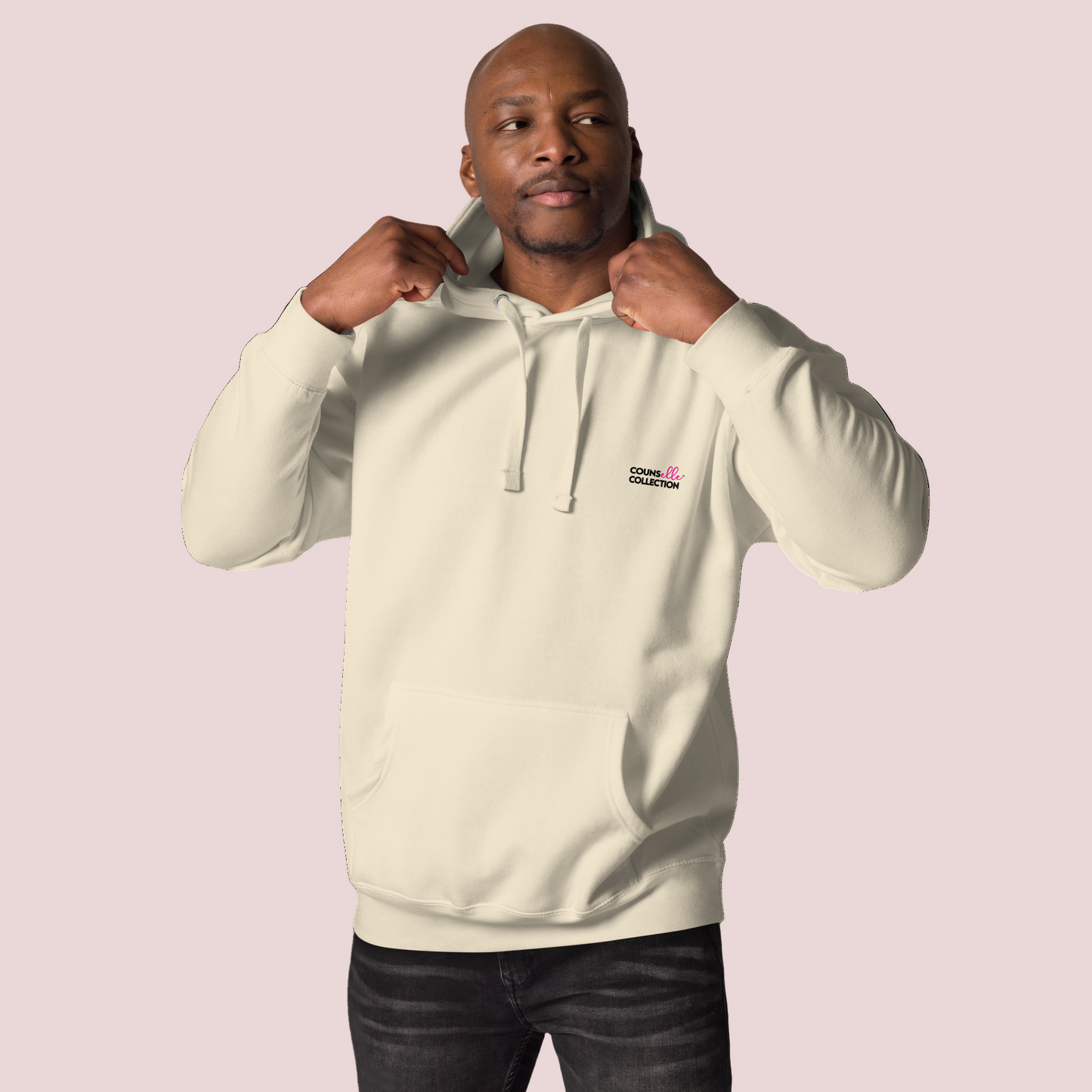 A black male model wearing a cream, long-sleeved hoodie featuring the counsellecollection logo on the left chest area.