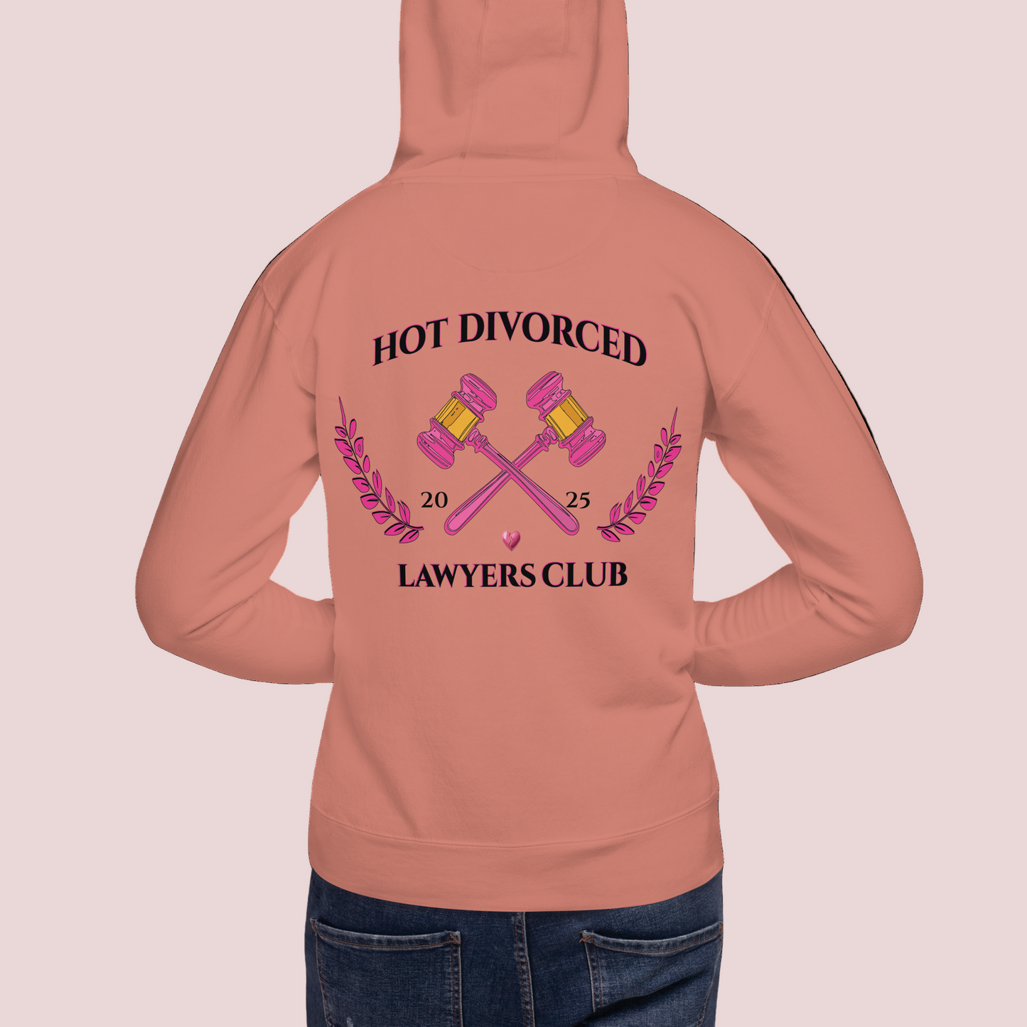 A model wearing a dusty rose colored, long-sleeved hoodie featuring the words "HOT DIVORCED LAWYERS CLUB 2025" with crossed gavels, laurel leaves, and a broken heart graphics.