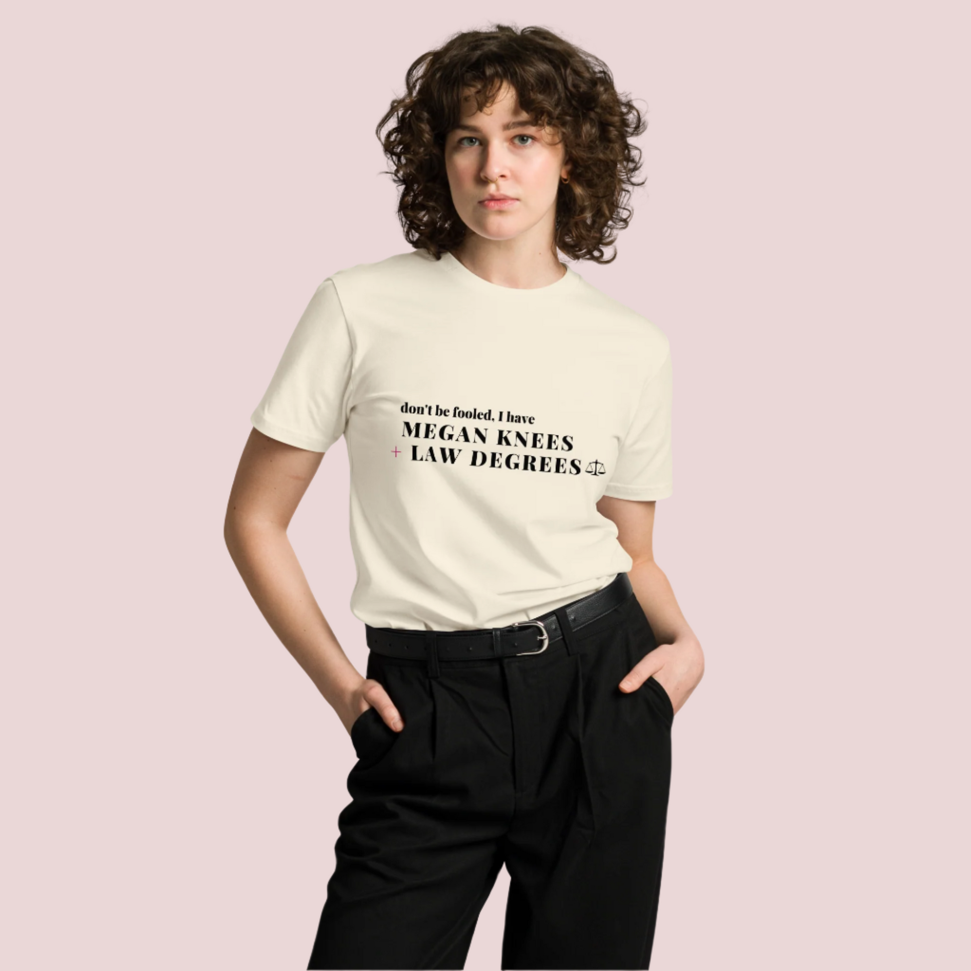  A model wearing black pants and a cream roundneck tee featuring the text: "DON'T BE FOOLED, I'VE GOT MEGAN KNEES + LAW DEGREES