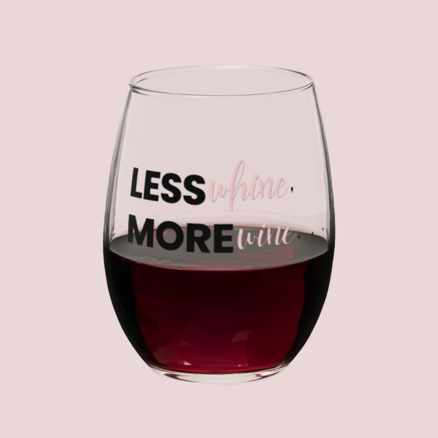 A clear, stemless wine glass with the words "Less WHINE, More WINE" written on it. Half-filled with red wine.