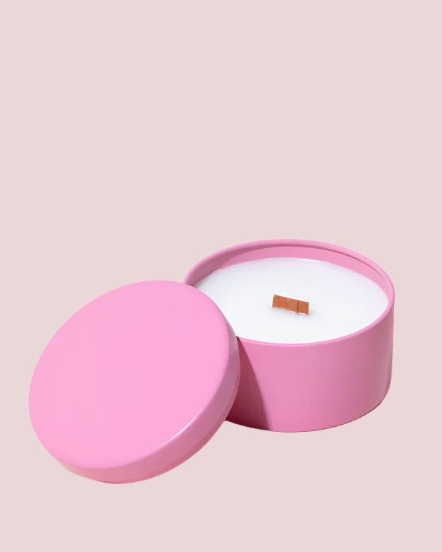 A candle in a plain pink tin container.