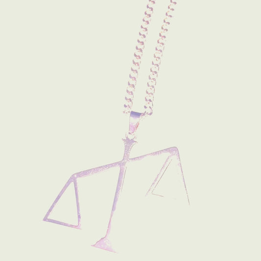 A gold chain necklace featuring a pendant in the shape of the scales of justice tipped to one side.