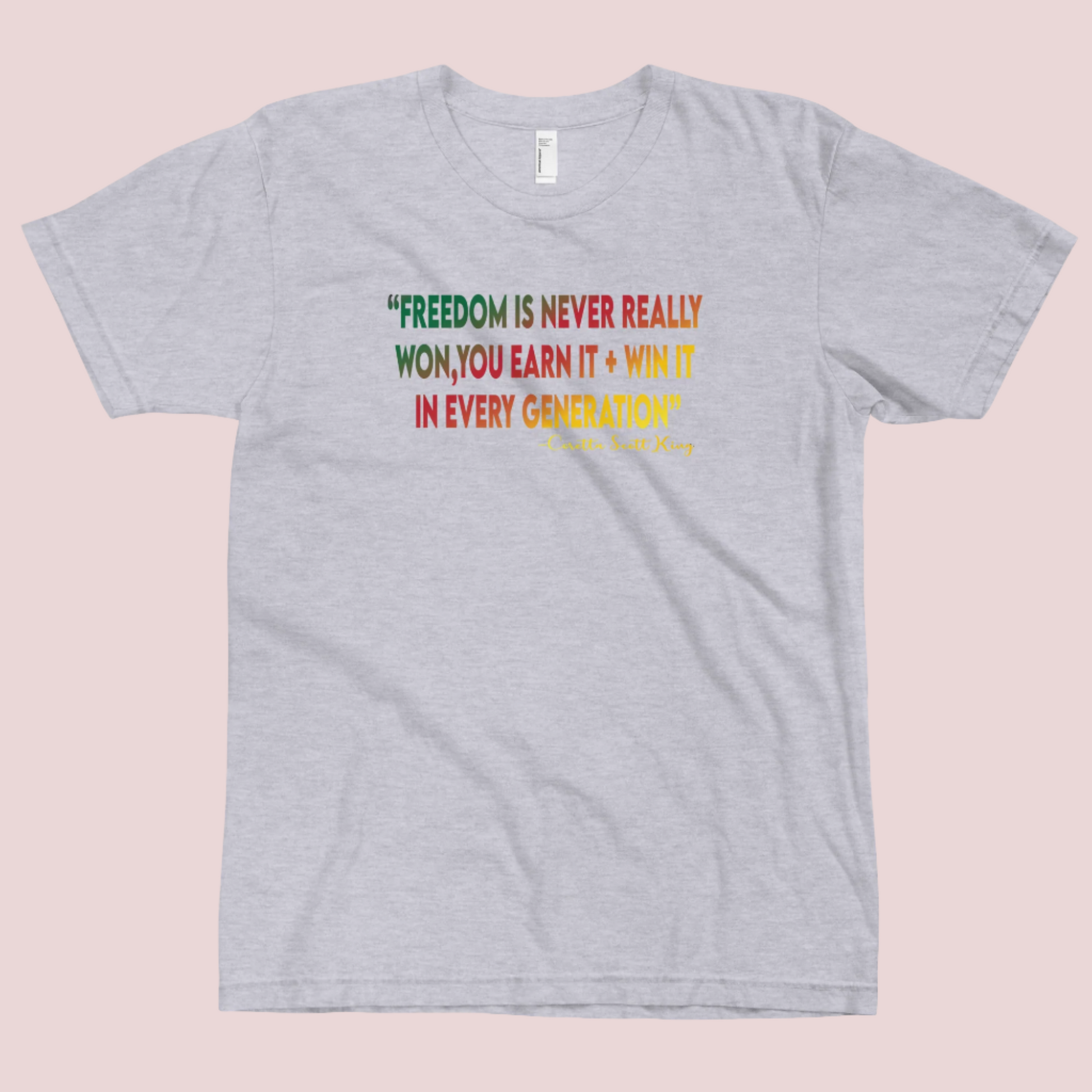 A grey roundneck tee featuring the quote "FREEDOM IS NEVER REALLY WON, YOU EARN IT + WIN IT In EVERY GENERATION" followed by the text "-Carlotta Scott King", all are written in green, red, and yellow striped font. 