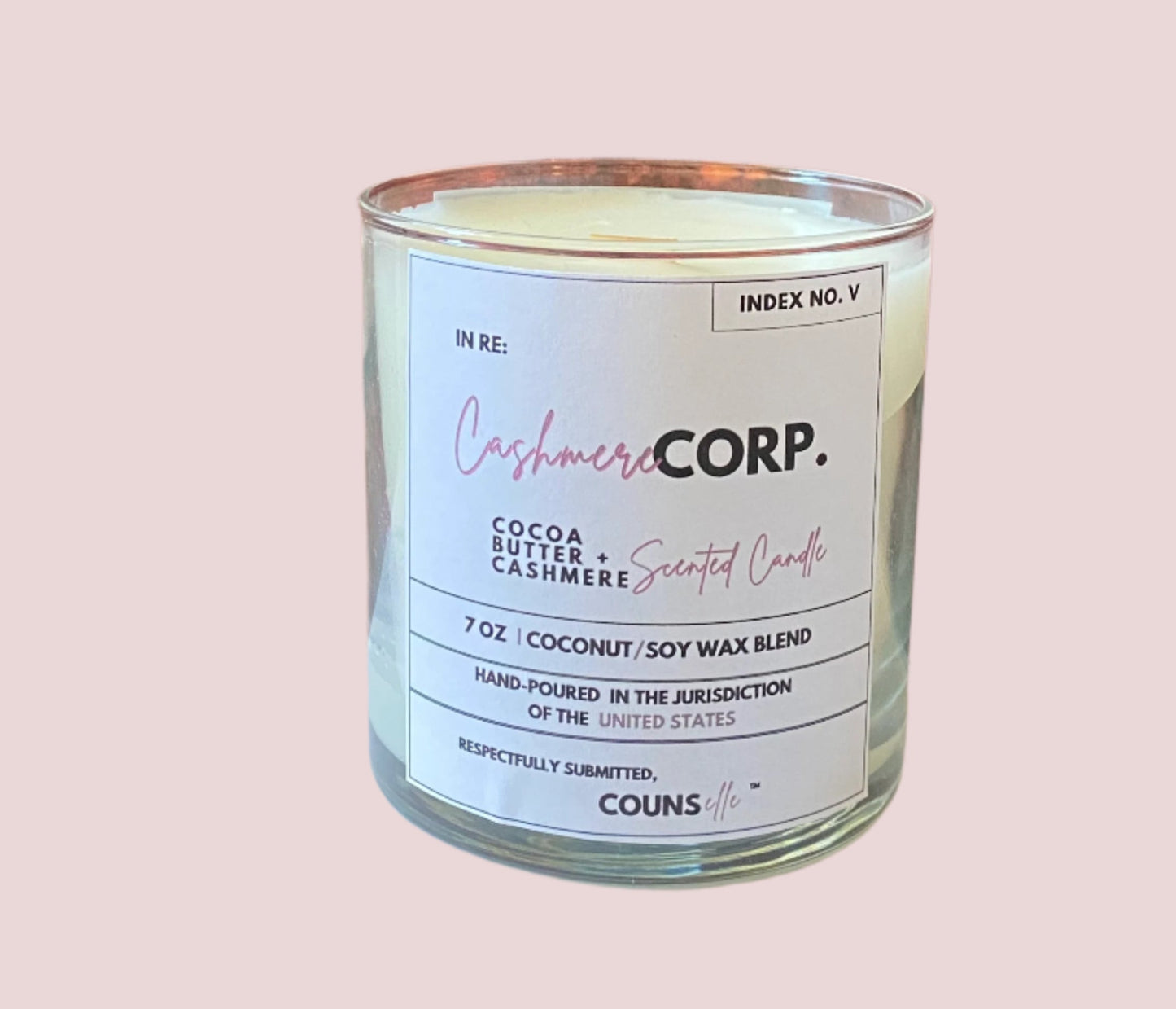 A candle in a glass container with a white label featuring the text "INDEX NO. V", "IN RE:", "CASHMERE CORP.", "COCOA BUTTER + CASHMERE SCENTED CANDLE", "7 oz", "COCONUT/SOY WAX BLEND", "HAND-POURED IN THE JURISDICTION OF THE UNITED STATES", "RESPECTFULLY SUBMITTED", with the counsellecollection logo at the bottom of the design