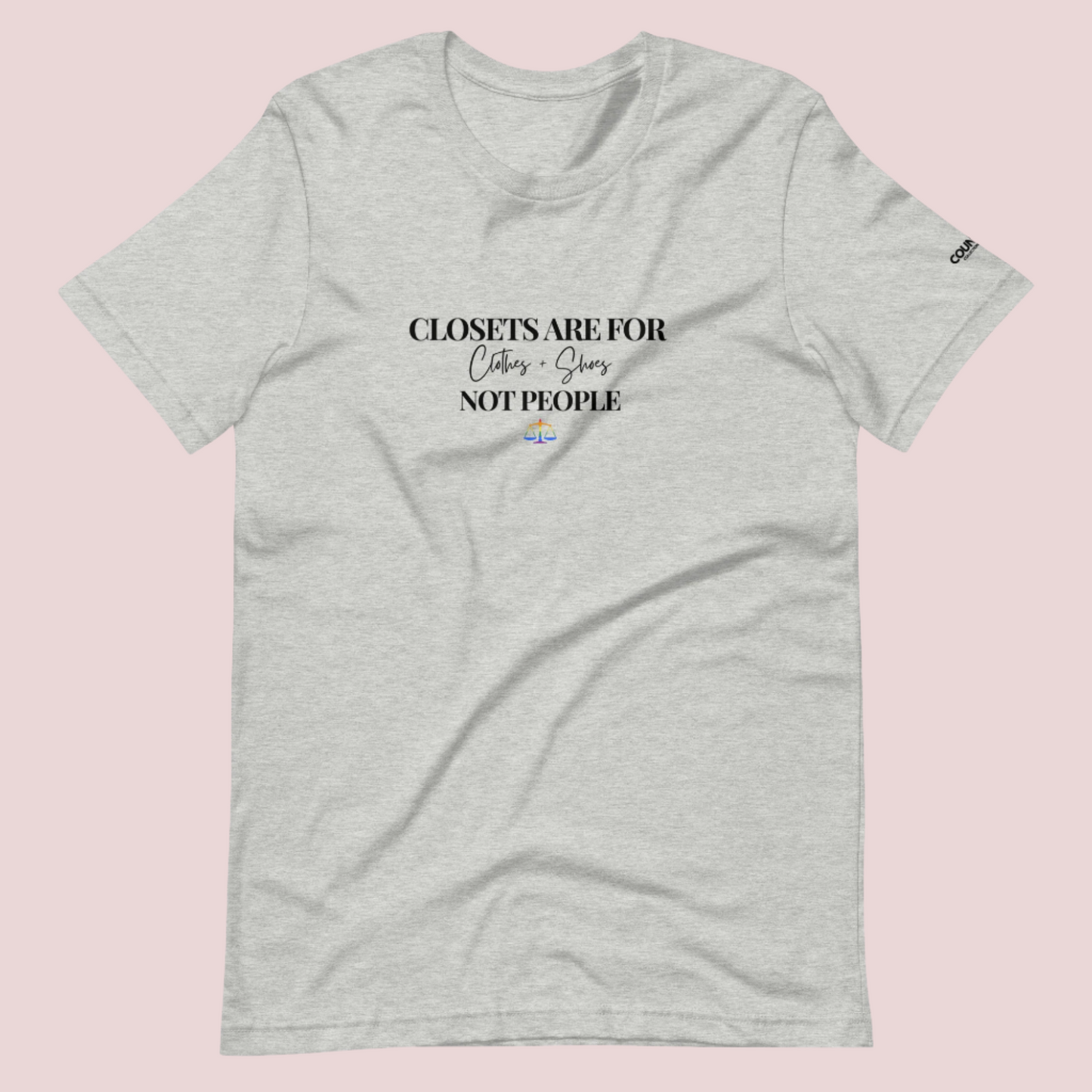  A grey crewneck tee with the text "CLOSETS ARE FOR CLOTHES + SHOES NOT PEOPLE" in black font, with an illustration of a rainbow justice scales underneath. The counsellecollection logo is seen on the left sleeve.