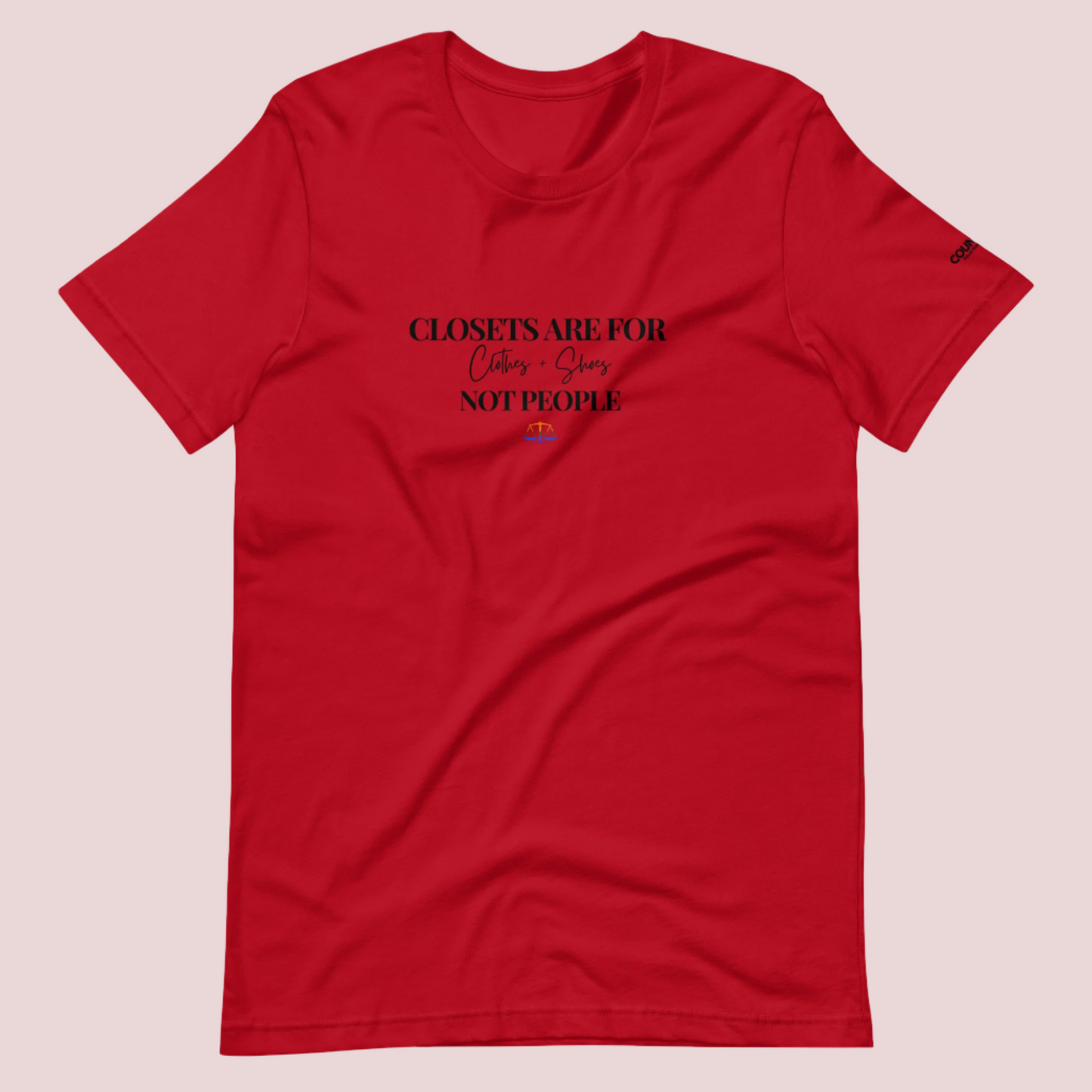  A red crewneck tee with the text "CLOSETS ARE FOR CLOTHES + SHOES NOT PEOPLE" in black font, with an illustration of a rainbow justice scales underneath. The counsellecollection logo is seen on the left sleeve.