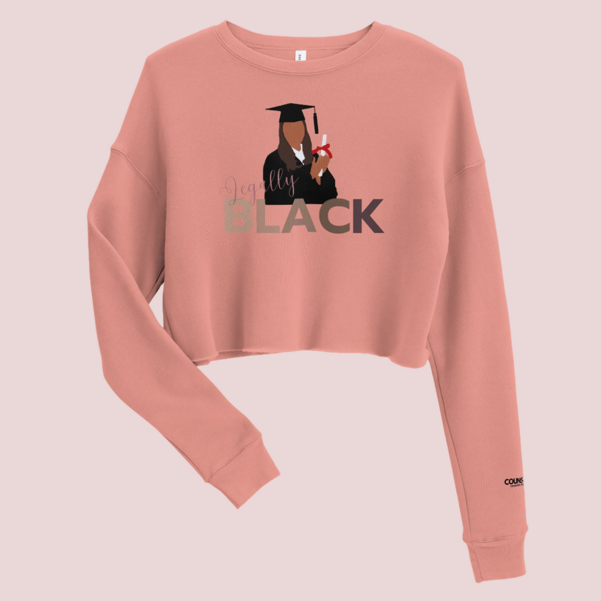 A rose roundneck, long-sleeved tee, with the text "Legally", in script, and "BLACK" in uppercase font and an illustration of a graduate student holding a diploma. The counsellecollection logo is seen on the left sleeve.