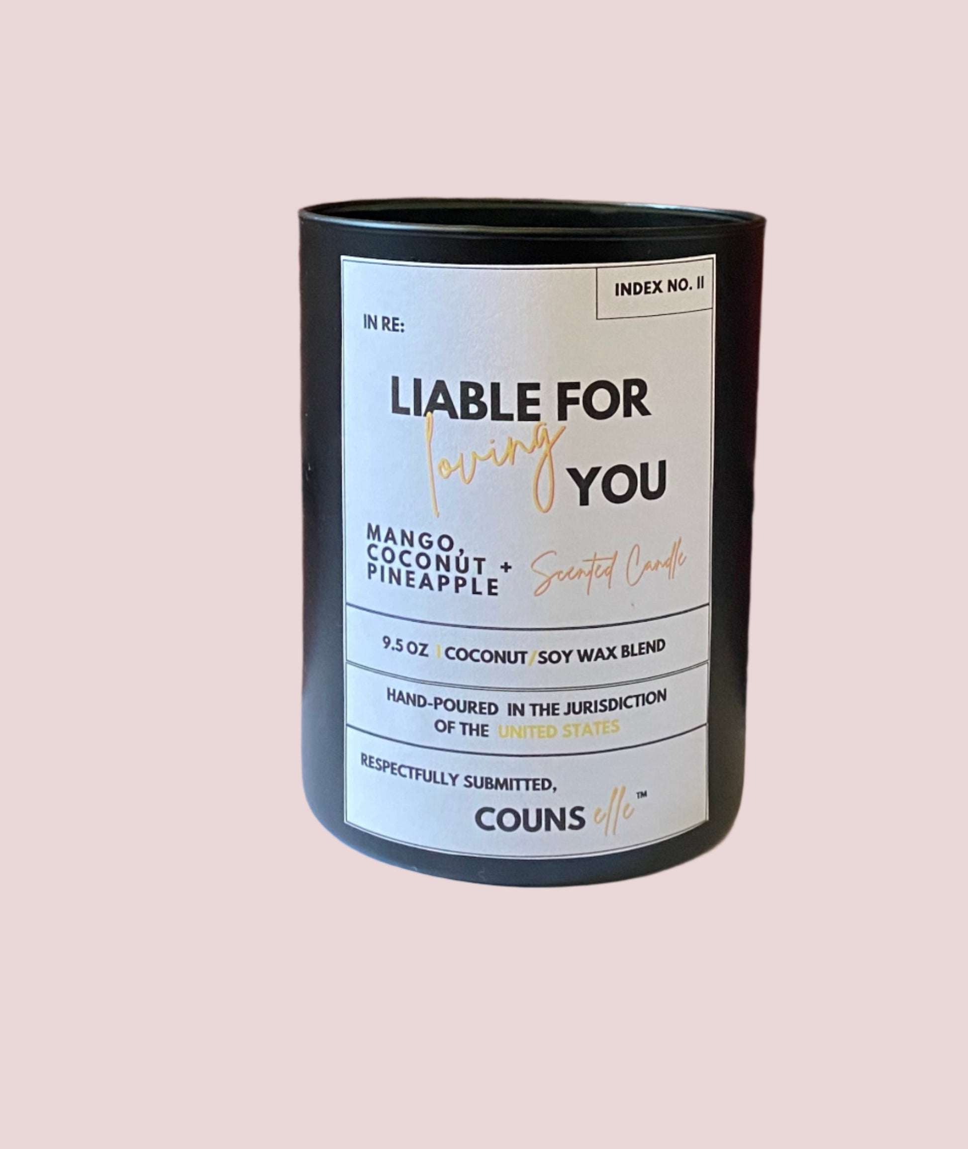 A candle in a black container with a white label featuring the text "INDEX NO. II", "IN RE:", "LIABLE FOR LOVING YOU", "MANGO, COCONUT + PINEAPPLE SCENTED CANDLE", "9.5 oz", "COCONUT/SOY WAX BLEND", "HAND-POURED IN THE JURISDICTION OF THE UNITED STATES", "RESPECTFULLY SUBMITTED", with the counsellecollection logo at the bottom of the design.