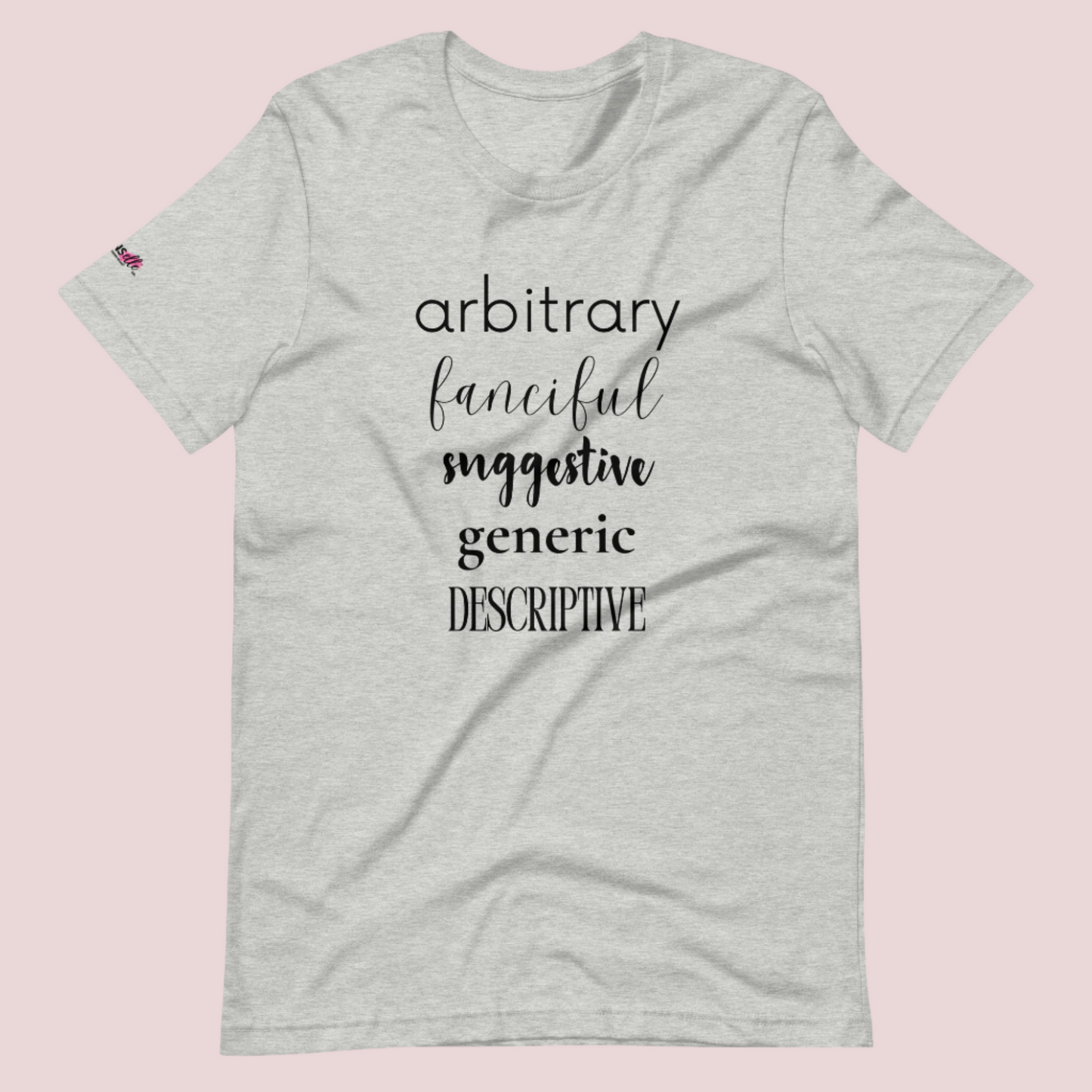 A heather grey roundneck tee featuring the words "arbitrary", "fanciful", "suggestive", "generic", and "descriptive" in different font styles, with the counsellecollection logo on a sleeve.