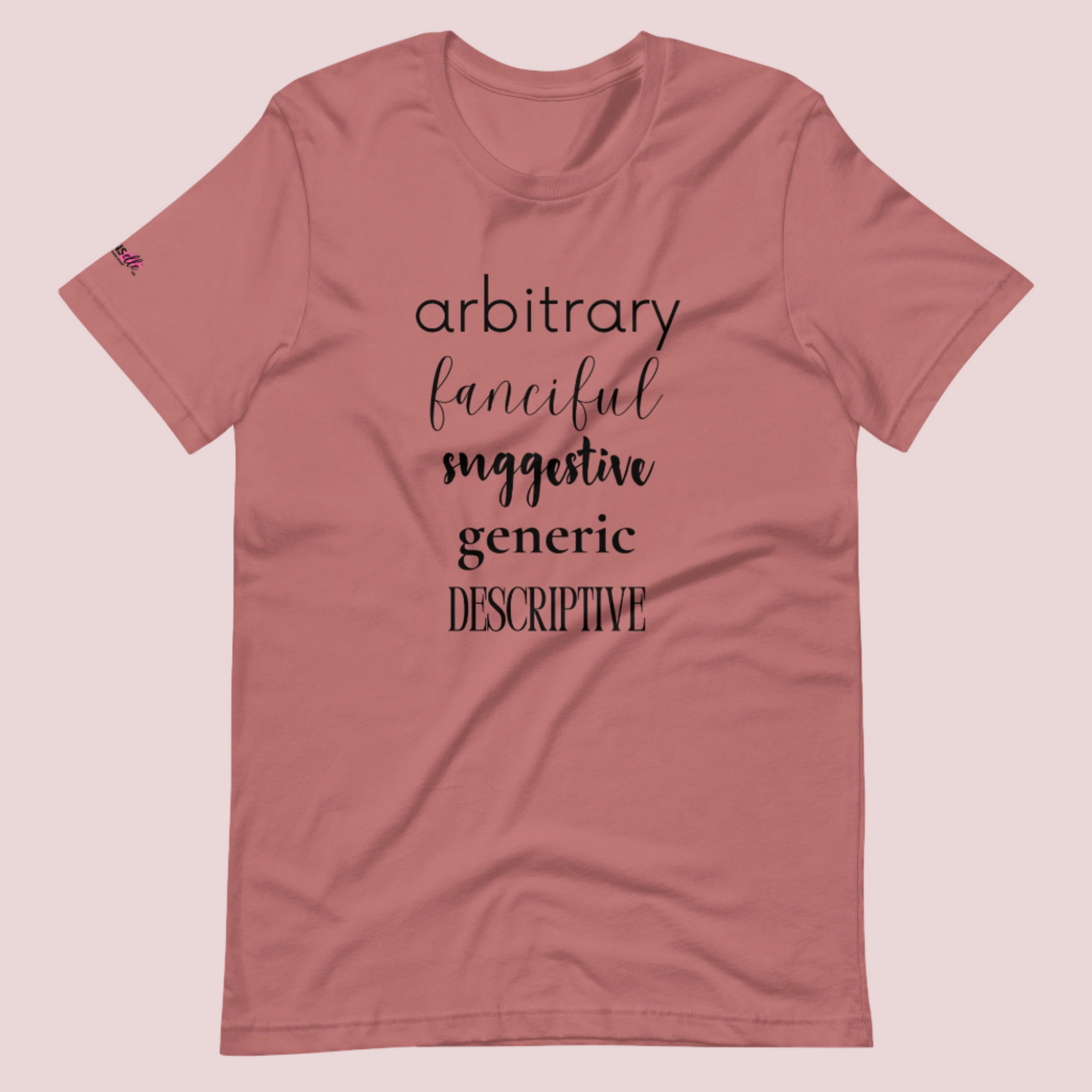 A mauve roundneck tee featuring the words "arbitrary", "fanciful", "suggestive", "generic", and "descriptive" in different font styles, with the counsellecollection logo on a sleeve.