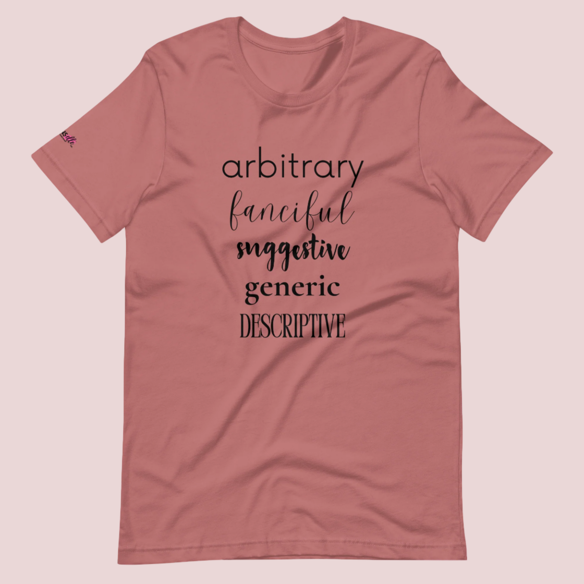 A mauve roundneck tee featuring the words "arbitrary", "fanciful", "suggestive", "generic", and "descriptive" in different font styles, with the counsellecollection logo on a sleeve.