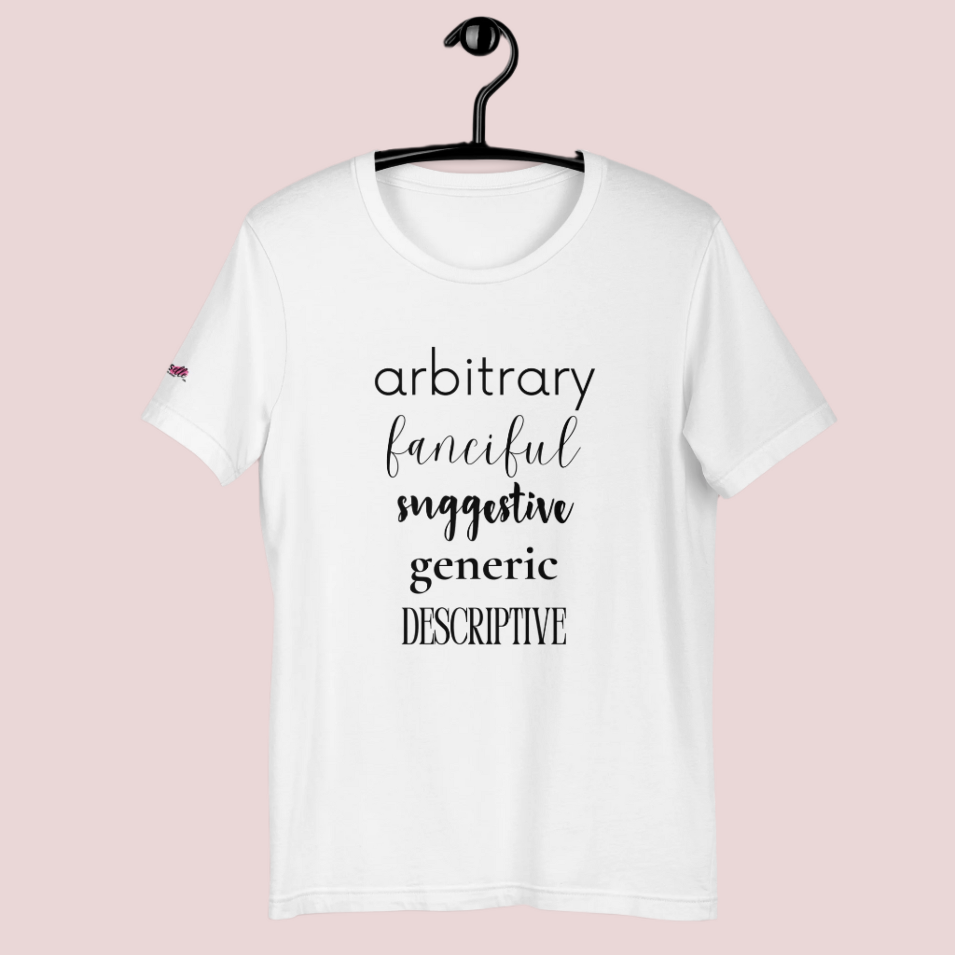 A white roundneck tee featuring the words "arbitrary", "fanciful", "suggestive", "generic", and "descriptive" in different font styles, with the counsellecollection logo on a sleeve.