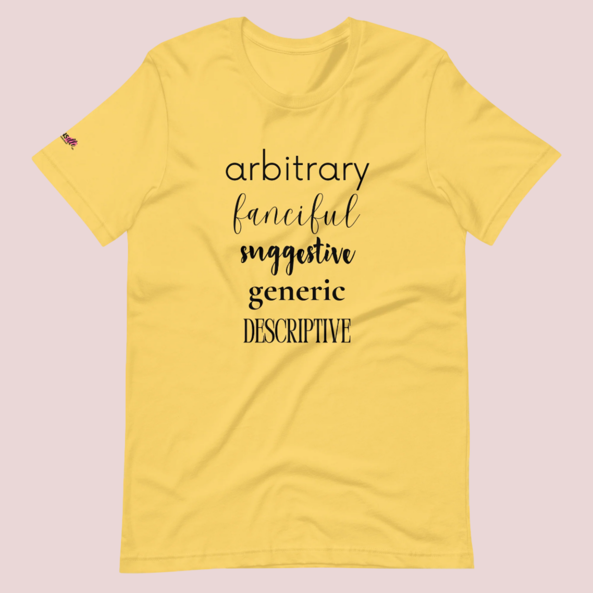 A yellow roundneck tee featuring the words "arbitrary", "fanciful", "suggestive", "generic", and "descriptive" in different font styles, with the counsellecollection logo on a sleeve.
