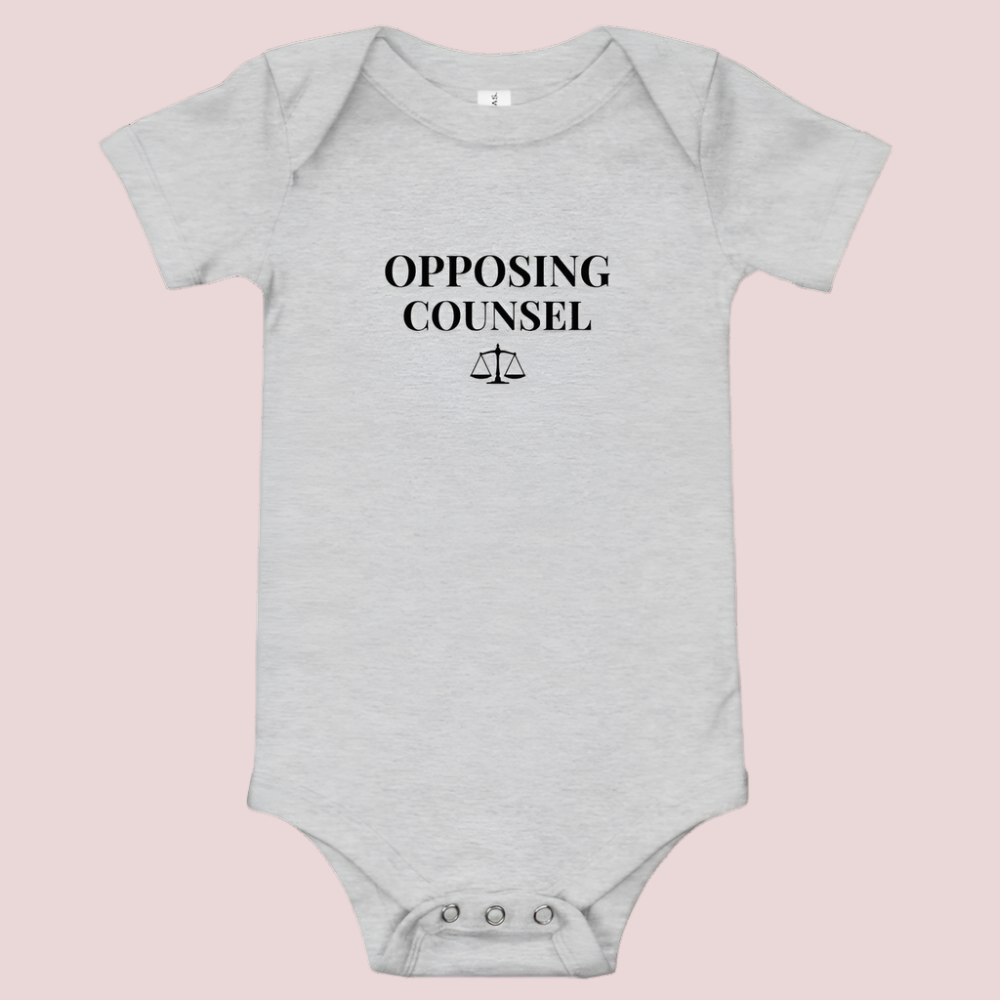 A grey infant onesie featuring in black text, the words "OPPOSING COUNSEL" and an illustration of justice scales.