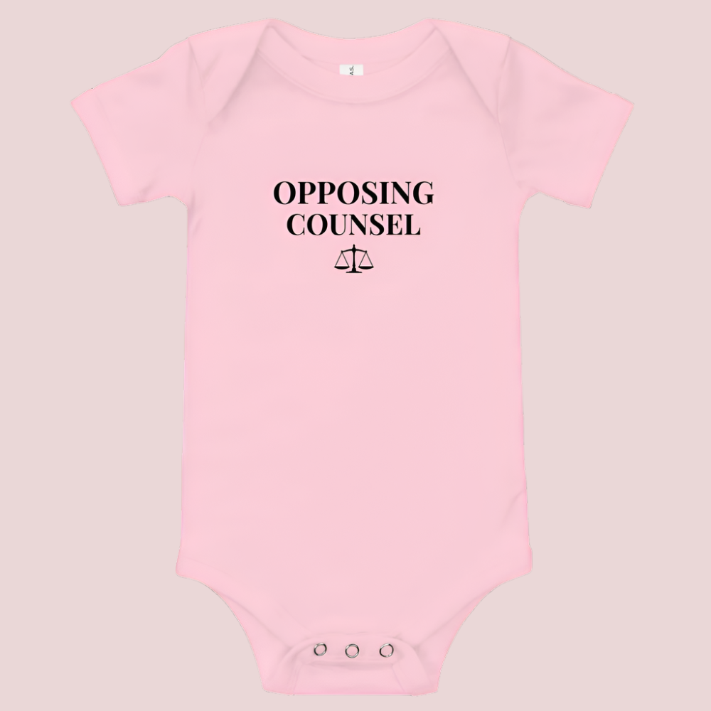 A pink infant onesie featuring in black text, the words "OPPOSING COUNSEL" and an illustration of justice scales.