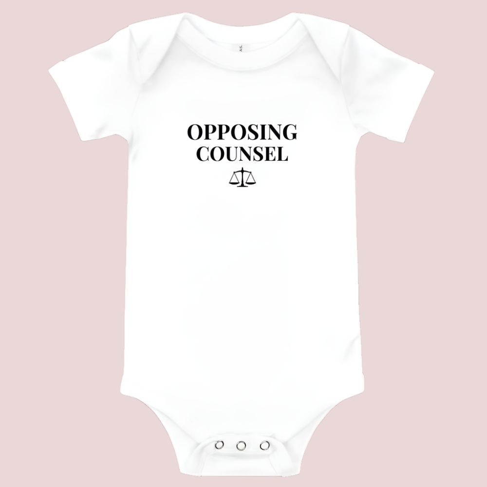 A white infant onesie featuring in black text, the words "OPPOSING COUNSEL" and an illustration of justice scales.