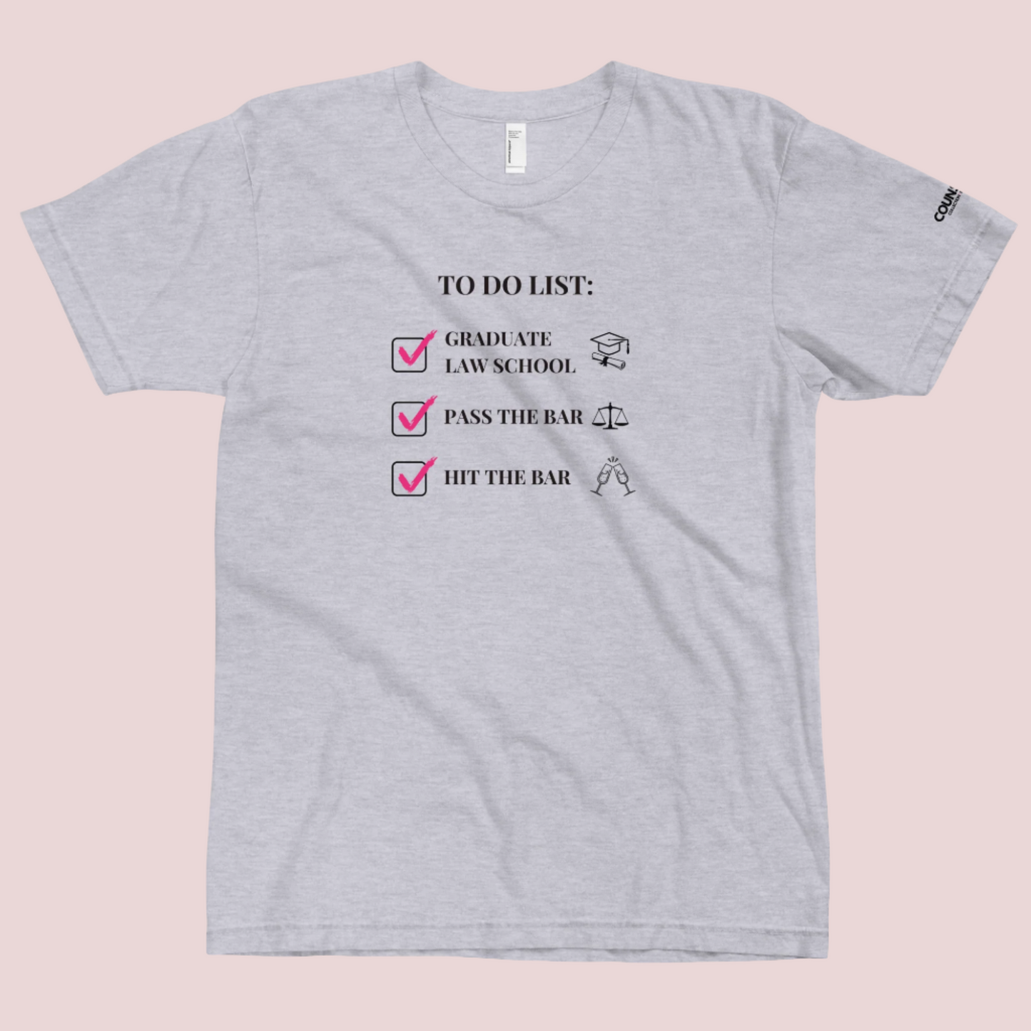 A grey crewneck tee showing the text "TO DO LIST", with ticked-off boxes beside the texts "GRADUATE LAW SCHOOL" and an illustration of a graduation cap and diploma; "PASS THE BAR" and an illustration of justice scales; and "HIT THE BAR" and an illustration of clinking champagne flutes, with the counsellecollection logo on the left sleeve.