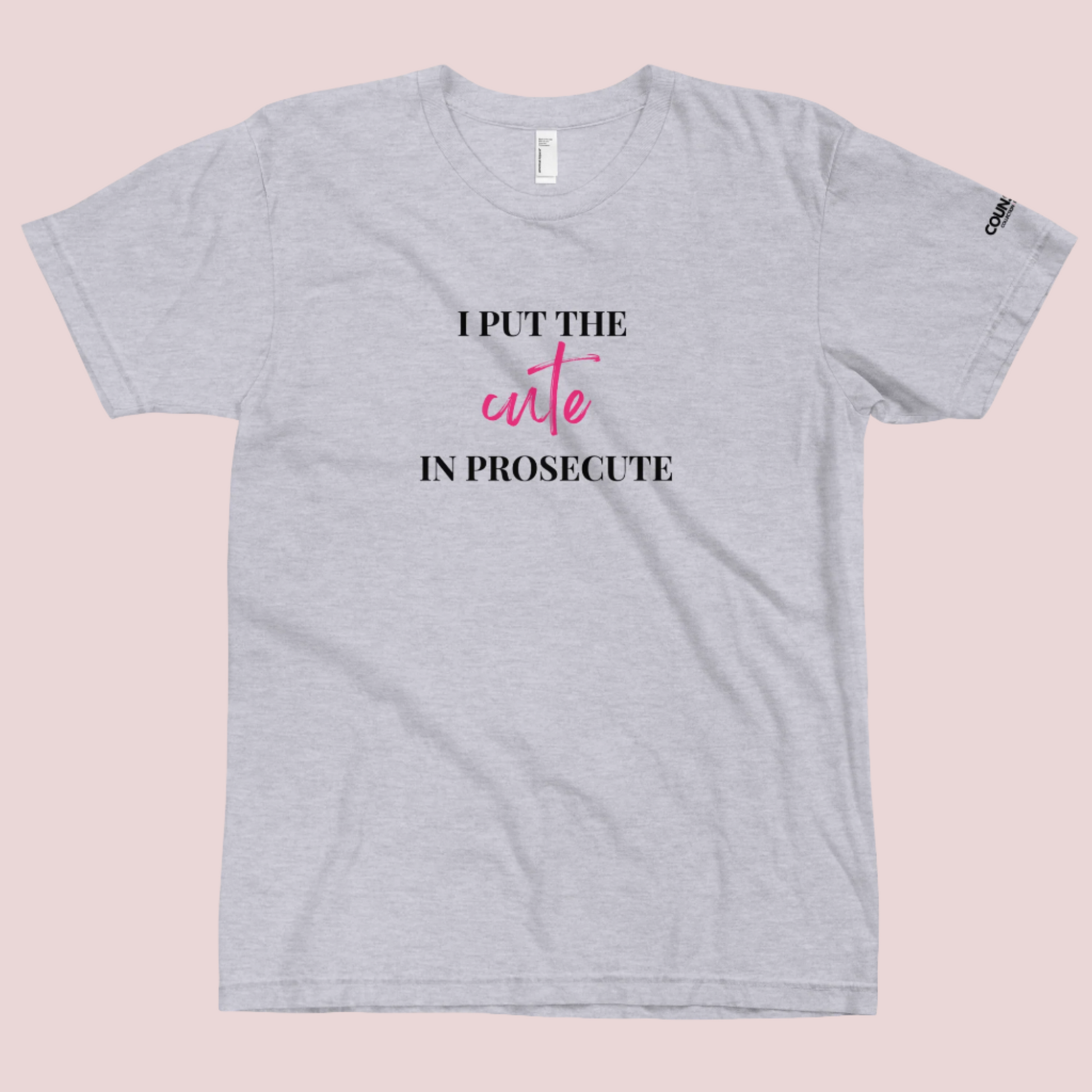 A heather grey round-neck tee with the text "I PUT THE CUTE IN PROSECUTE" and the counsellecollection logo on the left sleeve.