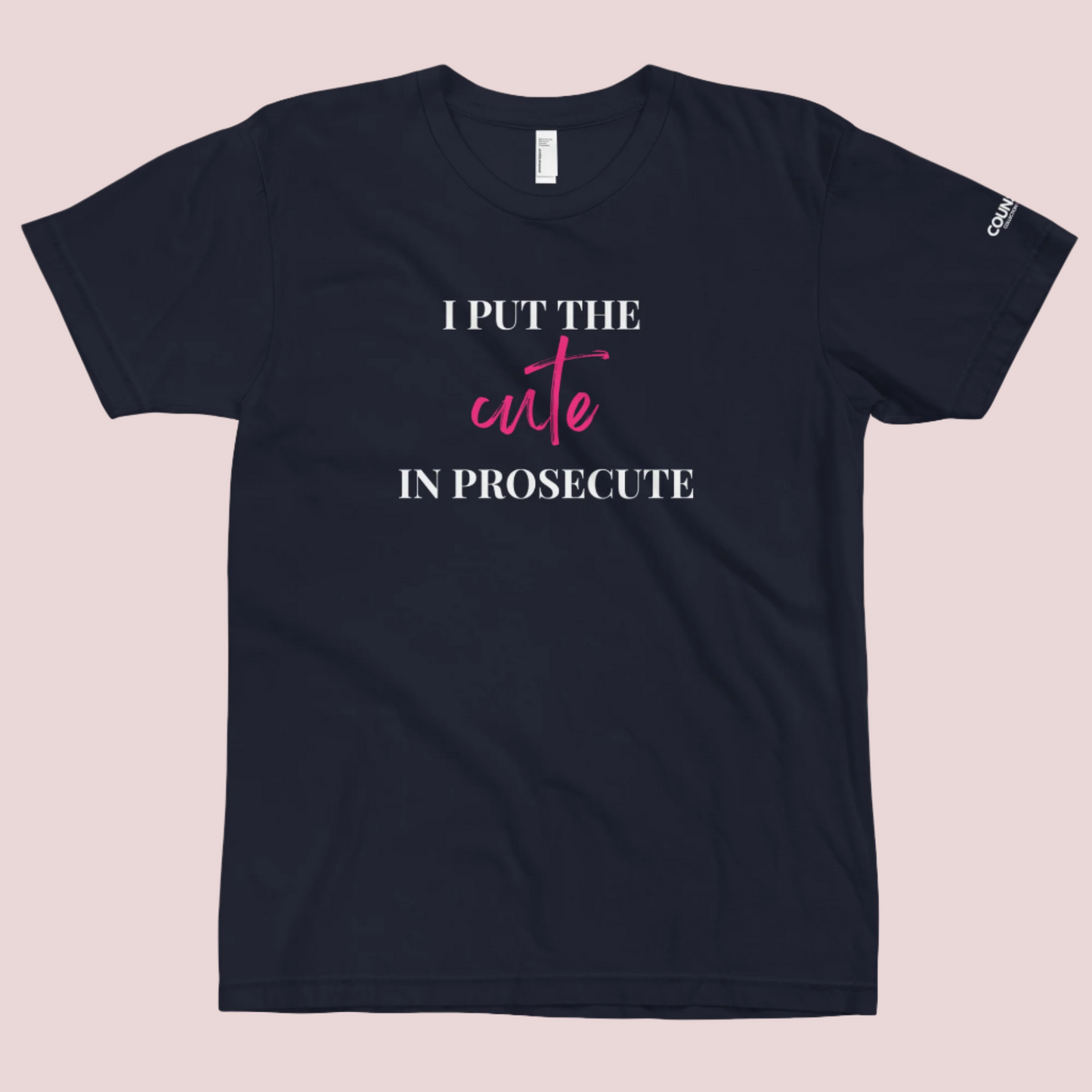 A navy blue round-neck tee with the text "I PUT THE CUTE IN PROSECUTE" and the counsellecollection logo on the left sleeve.