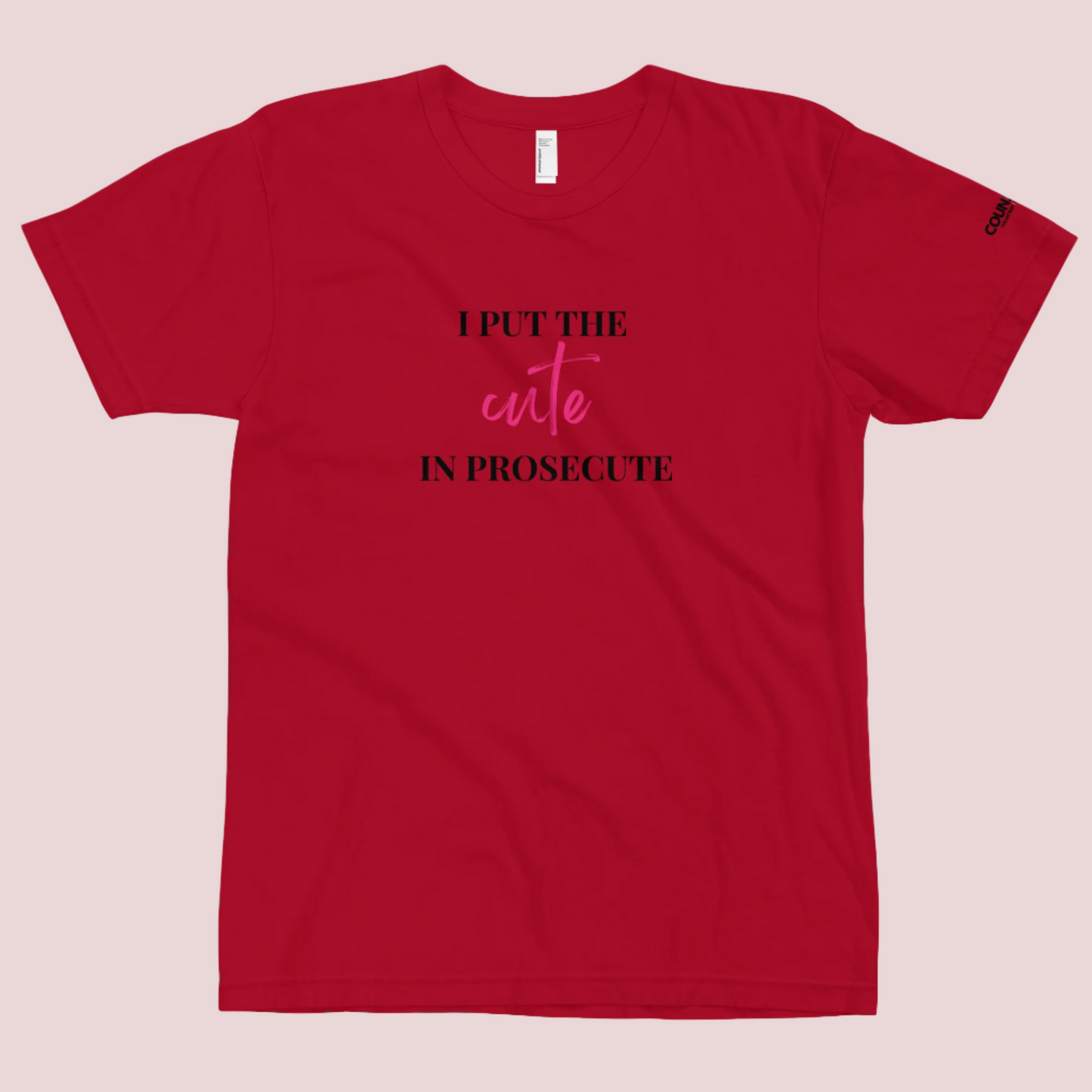 A red round-neck tee with the text "I PUT THE CUTE IN PROSECUTE" and the counsellecollection logo on the left sleeve.